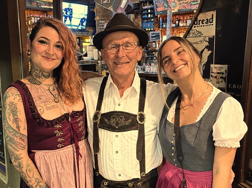 Gary Wenzlaff in lederhosen and a felt hat, smiling between two members of the pub staff in dirndls.